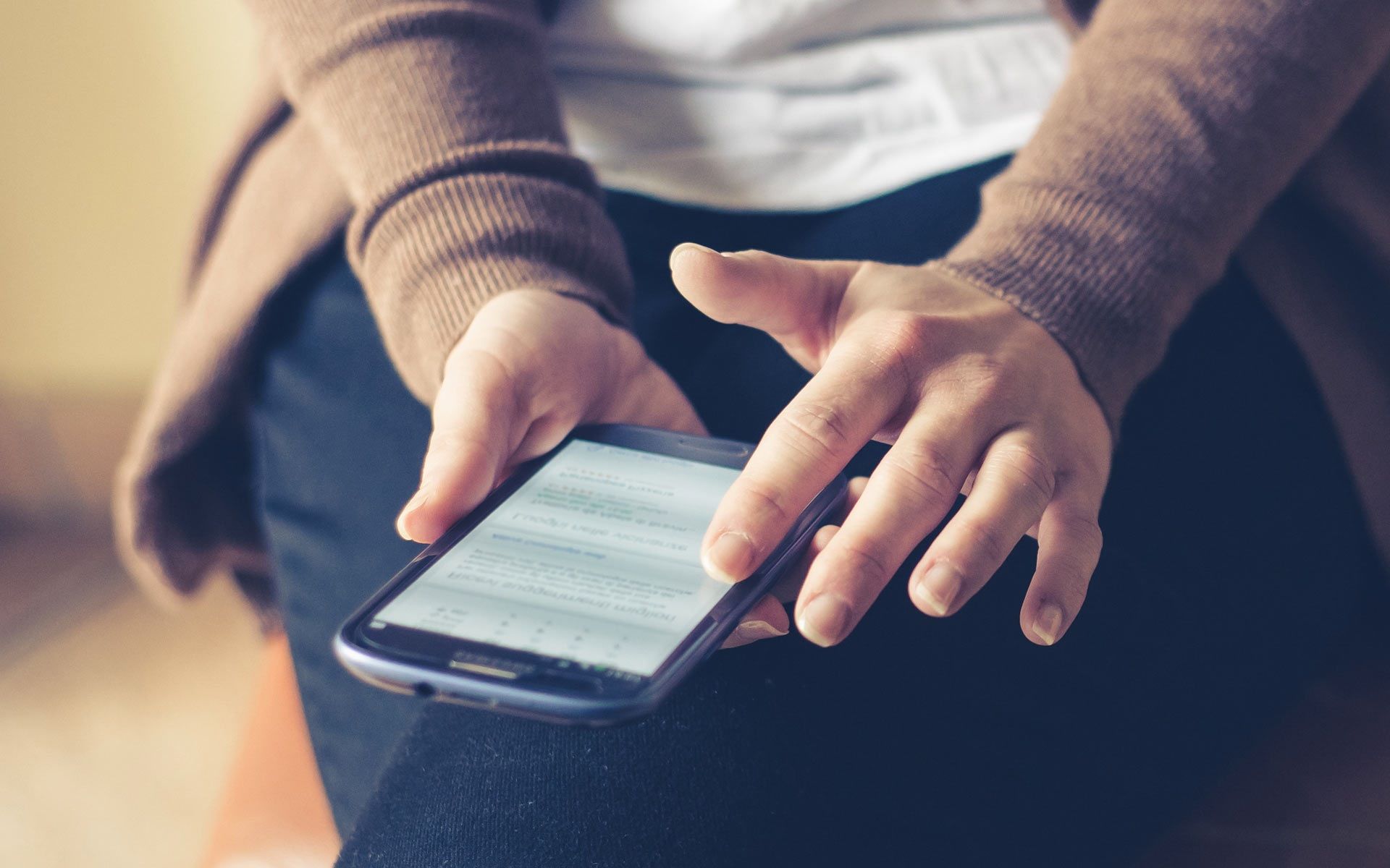 Person using a smartphone indoors, browsing the web with focus on the screen