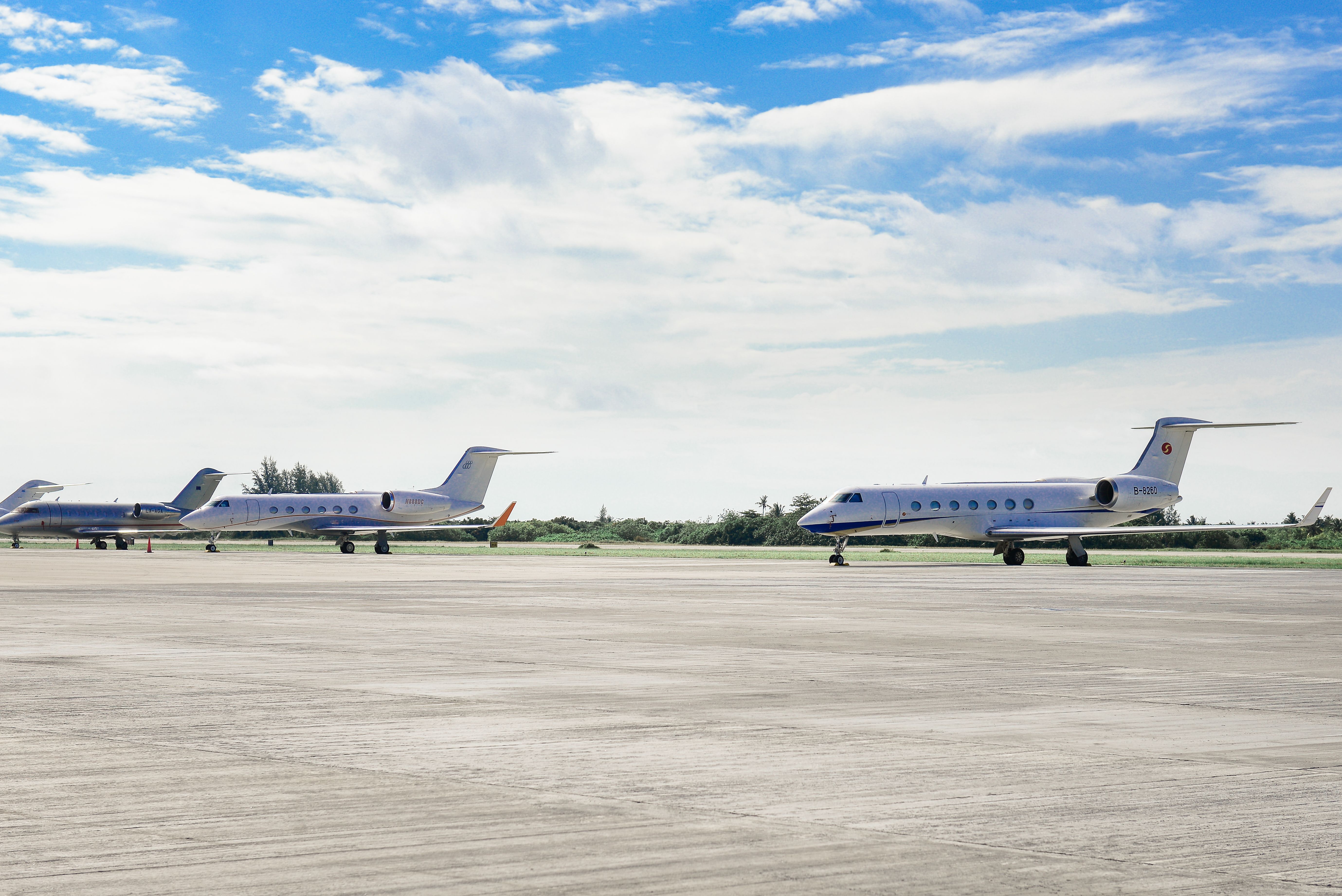 Row of private jets parked on an airport runway under a clear sky